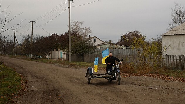 Uèitel Jurij Nevolèuk jede na motocyklu s národními vlajkami ve vesnici Blahodatne v Chersonské oblasti, kterou znovu dobyla ukrajinská armáda. (11. listopadu 2022)